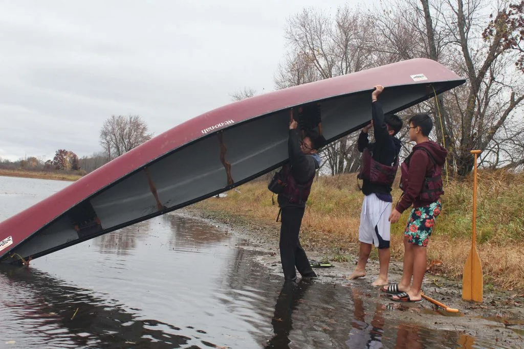 students lifting a canoe into the water