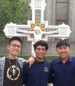 3 students in front of a cross